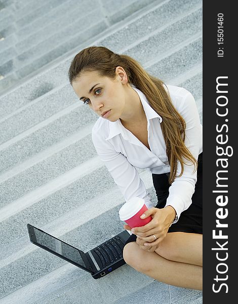 Young, beautiful woman business over coffee in the fresh air sitting on the stairs, office building, next to the laptop. Young, beautiful woman business over coffee in the fresh air sitting on the stairs, office building, next to the laptop.