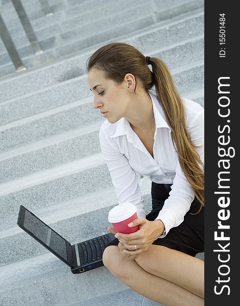 Young, beautiful woman business over coffee in the fresh air sitting on the stairs, office building, next to the laptop. Young, beautiful woman business over coffee in the fresh air sitting on the stairs, office building, next to the laptop.