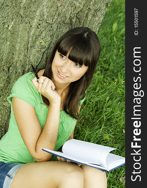 Young beautiful woman in a park with a notebook and pen. Young beautiful woman in a park with a notebook and pen