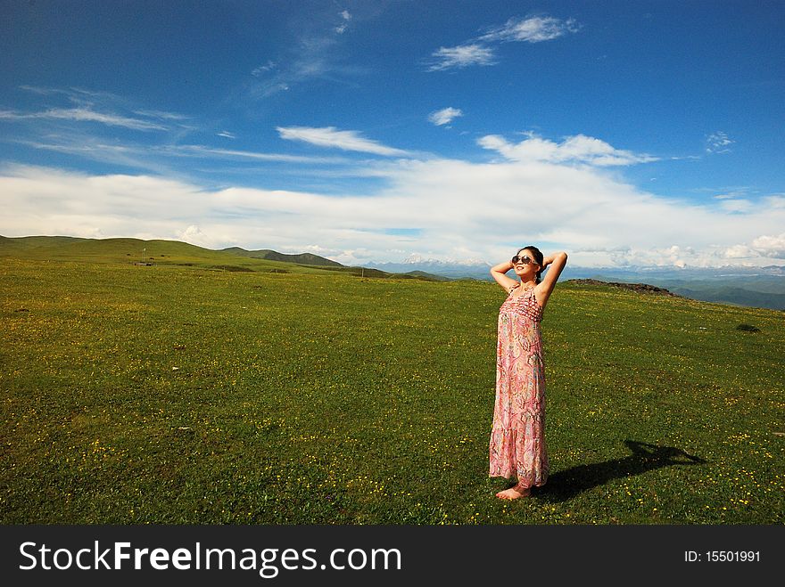 Girl is standing under the blue sky on the grassland.