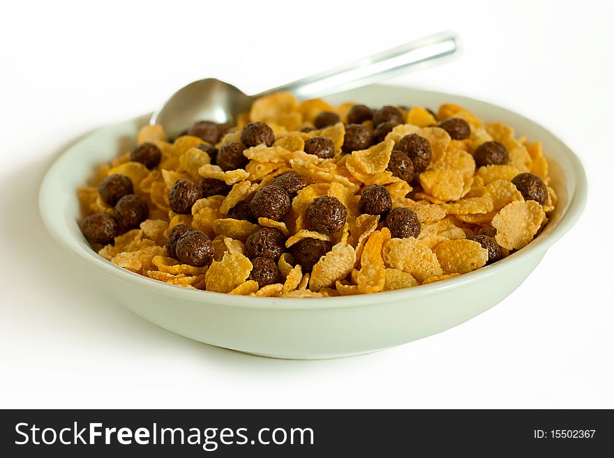 Cornflakes, cocoa balls and spoon in a bowl isolated on white. Cornflakes, cocoa balls and spoon in a bowl isolated on white.
