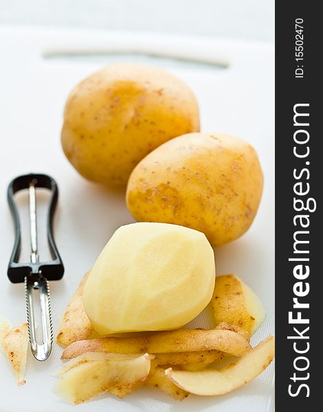 Potatoes and a peeler on a chopping board