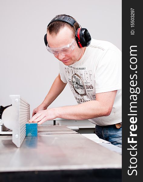 Carpenter working on an electric buzz saw cutting some boards, he is wearing safety glasses and hearing protection to make things safe