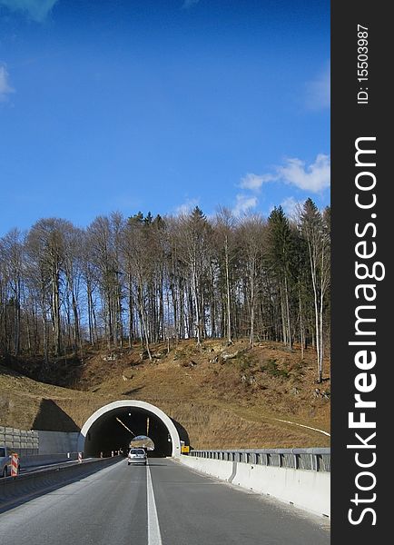Highway road and a short tunnel under the forested hill, with bright blue skies and space for text (copypsace). Highway road and a short tunnel under the forested hill, with bright blue skies and space for text (copypsace)