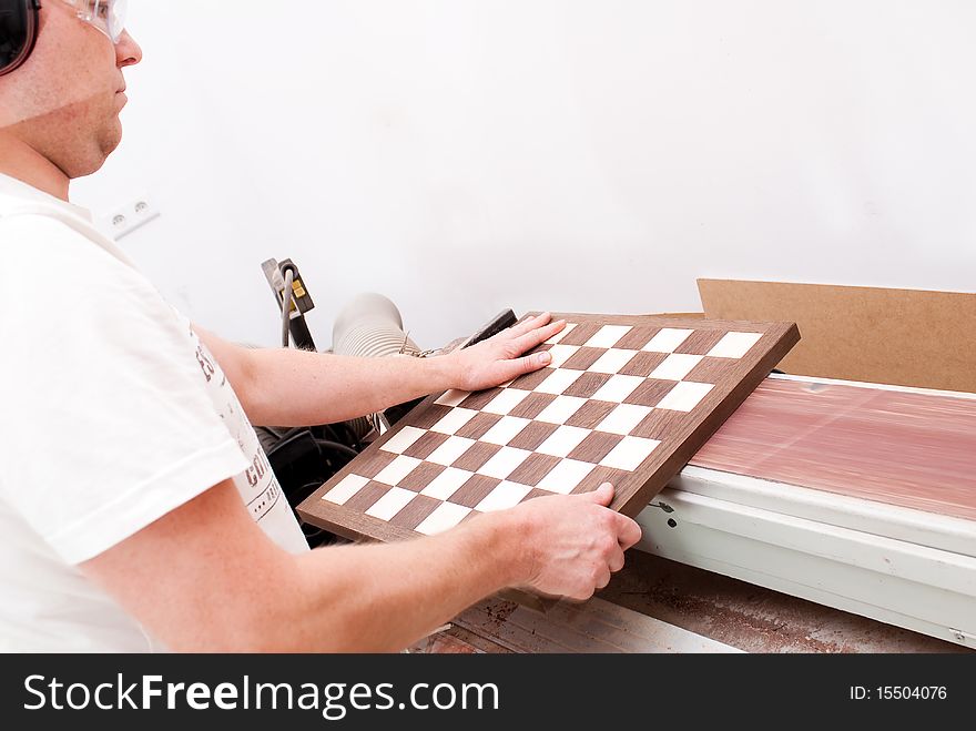 Carpenter working on an electric buzz saw cutting some chess boards