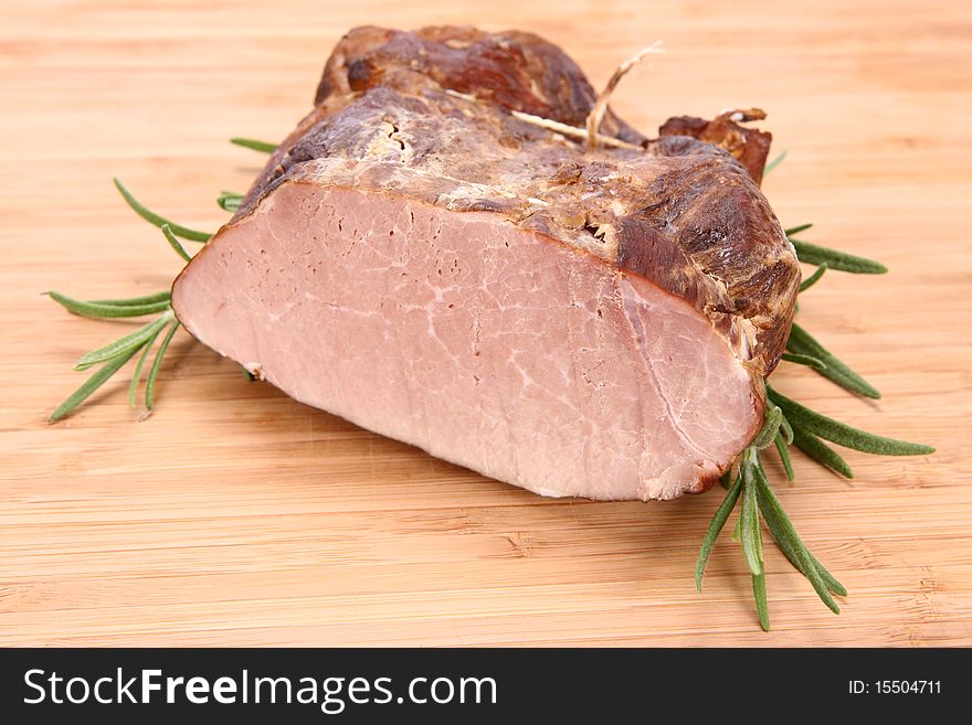 Piece of ham decorated with rosemary on a wooden background