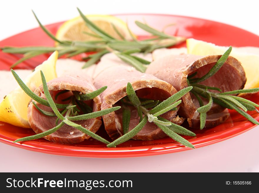 Rolled slices of ham filled with rosemary on a plate decorated with lemon