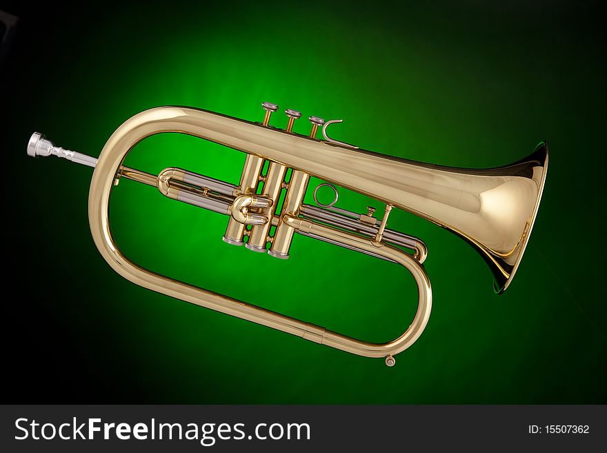 A gold flugalhorn trumpet isolated against a spotlight green background. A gold flugalhorn trumpet isolated against a spotlight green background.