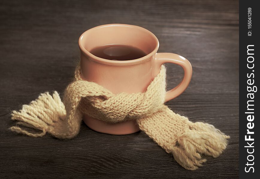Healing cup of tea in a scarf on a wooden background.
