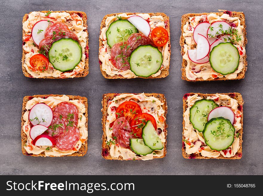 Sandwiches with cream cheese, vegetables and salami. Sandwiches with cucumber, radish, tomatoes, salami on a gray background, top view. Flat lay