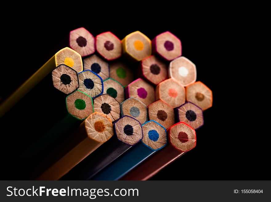 Wooden pencils in all colors seen at the base of pencils. Colored pencils stacked. With a black background.Colors. Back to school