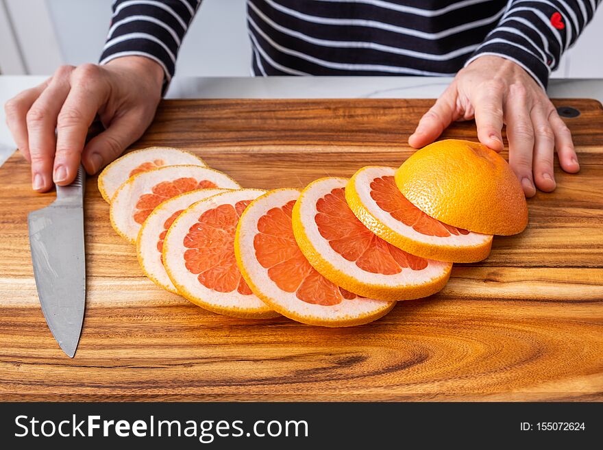 Wooden chopping board with sliced red grapefruit.
