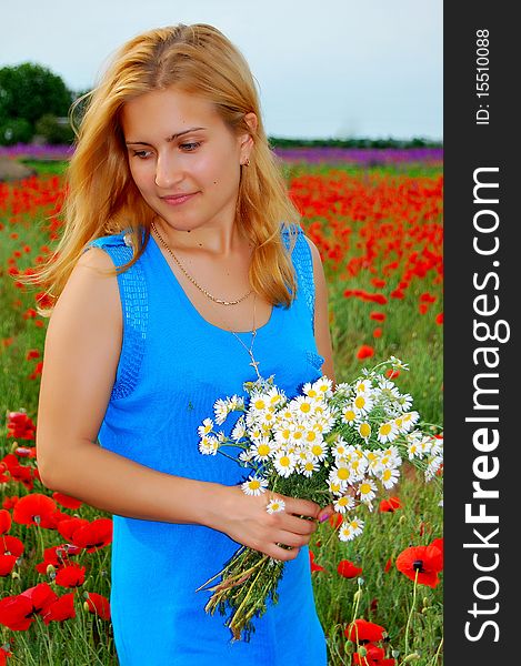 A beautiful girl is holding camomiles and walking on the poppy field