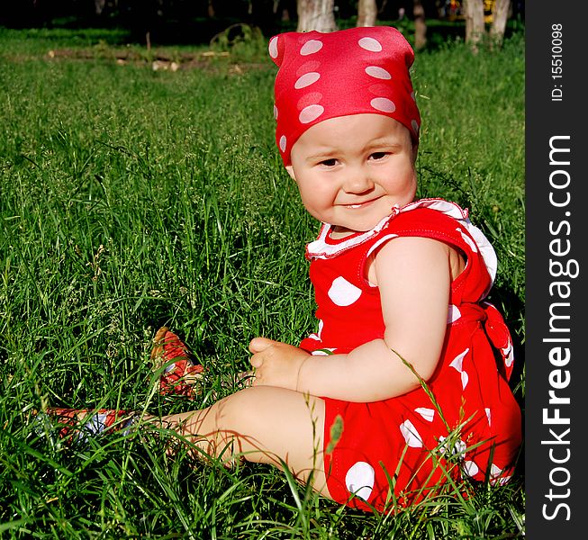 Baby is a red and white dress sitting on the grass. Baby is a red and white dress sitting on the grass