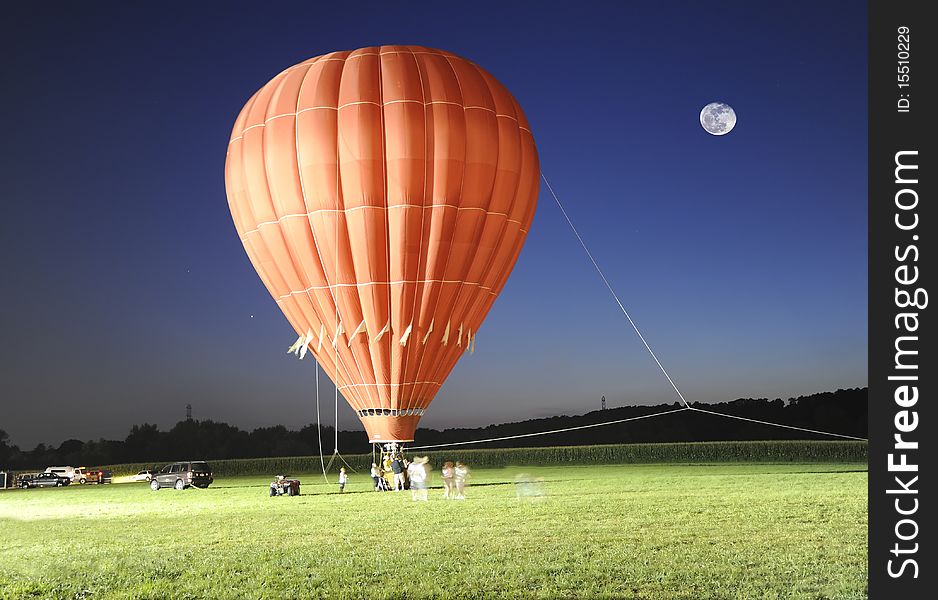 A red hot air balloon photographed at night. Note the full moon, blue sky and green grass. A red hot air balloon photographed at night. Note the full moon, blue sky and green grass