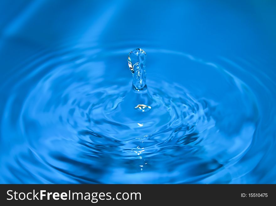 Clean blue drop of water splashing in clear water. Abstract blue background