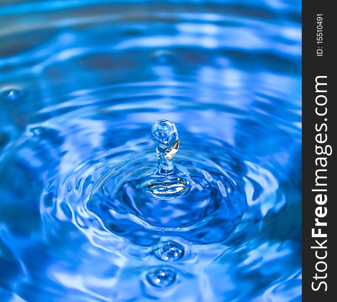 Clean blue drop of water splashing in clear water. Abstract blue background