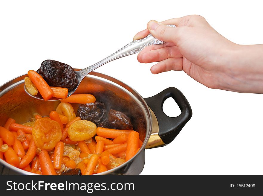 A hand taking off the stewed baby carrots with dried fruits from the pan isolated on white