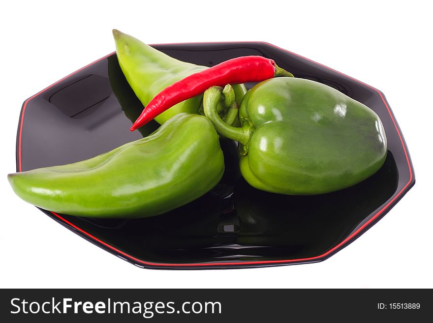 Three green peppers and red chili on the black plate isolated on white