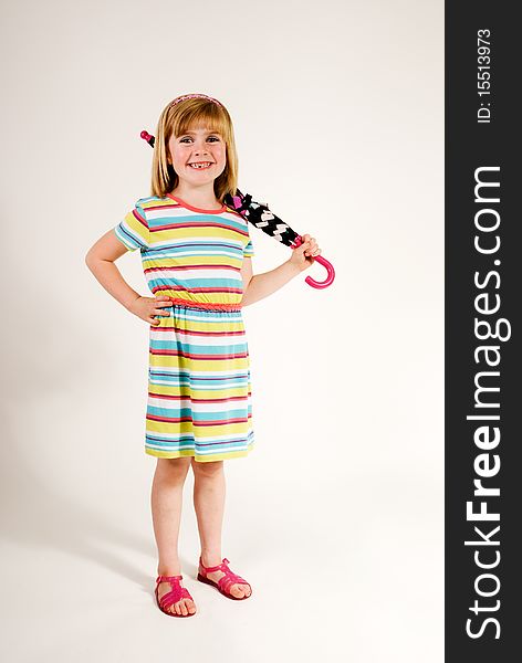 A vertical image of a lovely and cute little girl standing in her sundress and sandles with a rolled up umbrella over her sholder and a lovely smile isolated against a plain background. A vertical image of a lovely and cute little girl standing in her sundress and sandles with a rolled up umbrella over her sholder and a lovely smile isolated against a plain background