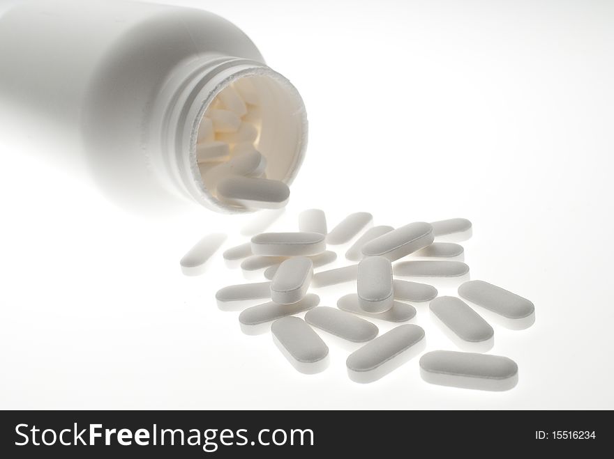 Close up of prescription medicine pills pouring out of white bottle on white background. Close up of prescription medicine pills pouring out of white bottle on white background