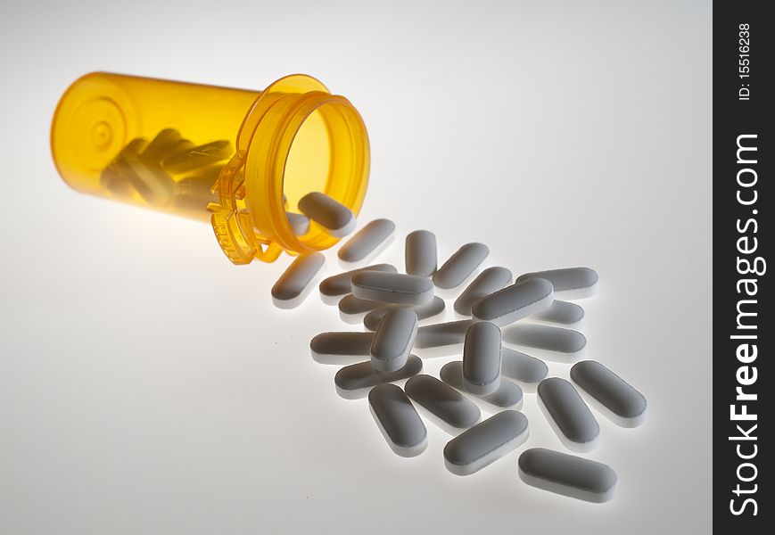 Close up of prescription medicine pills pouring out of orange bottle on white background. Close up of prescription medicine pills pouring out of orange bottle on white background