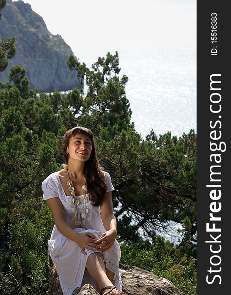 Young girl in white dress sitting on the rock on the nature background. Young girl in white dress sitting on the rock on the nature background