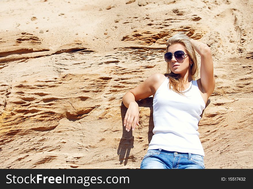 Young girl the blonde in jeans, against sand