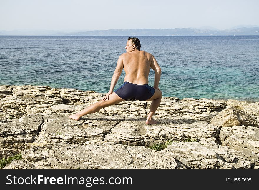 Color landscape photo of a caucasian man stretching on rocky beach