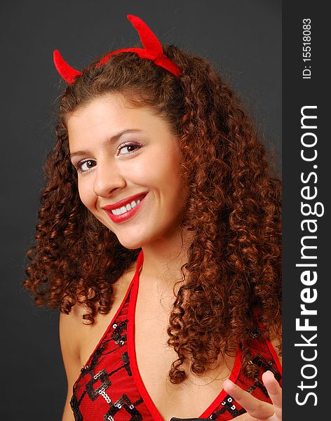 woman is smiling broadly and looking at the camera. Small red horns are in her curly hair. woman is smiling broadly and looking at the camera. Small red horns are in her curly hair
