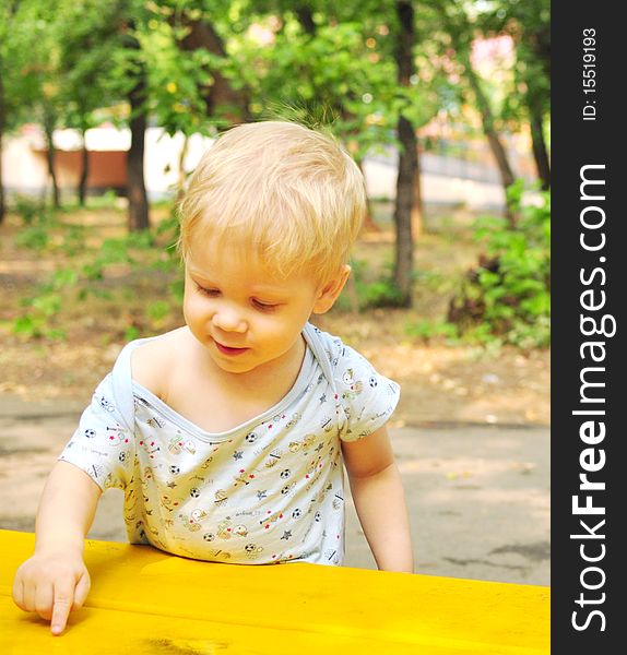 Little handsome boy draws a finger on the yellow bench. Little handsome boy draws a finger on the yellow bench