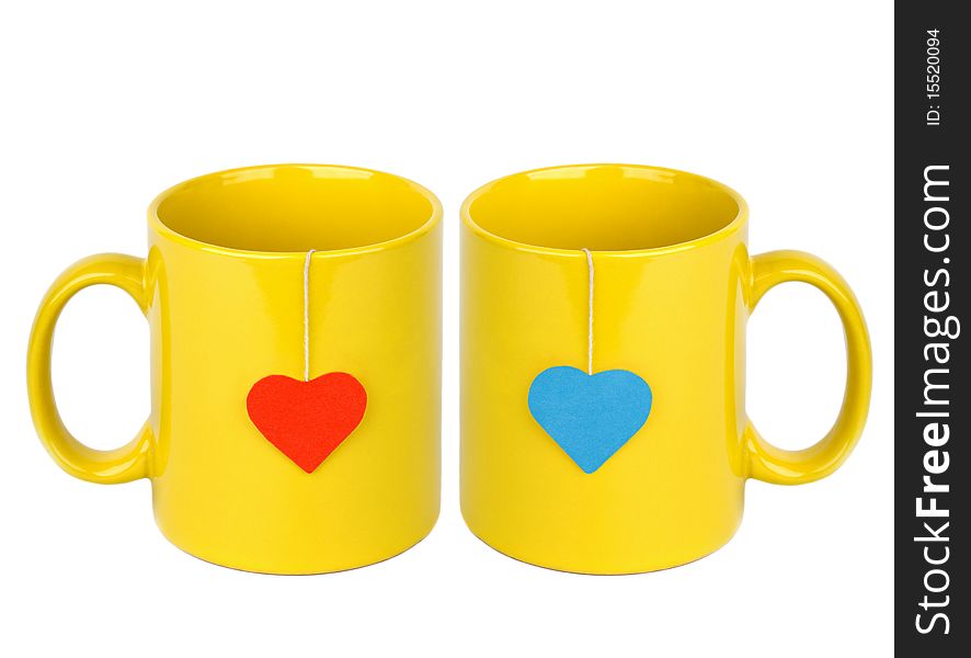 Tea bags with red and blue heart-shaped lables in yellow cups isolated on white. Tea for two. Tea bags with red and blue heart-shaped lables in yellow cups isolated on white. Tea for two