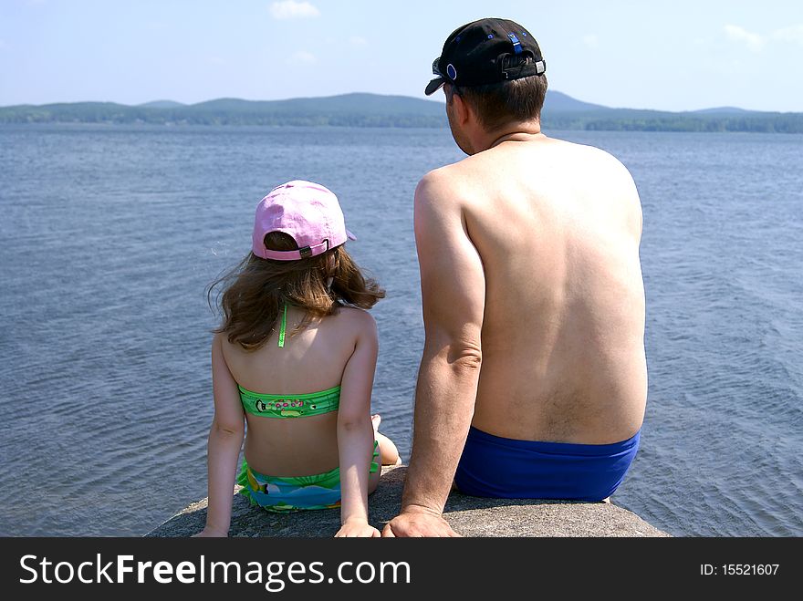 The man in swimming trunks and the girl in a bathing suit sit having turned a back ashore at water. The man in swimming trunks and the girl in a bathing suit sit having turned a back ashore at water