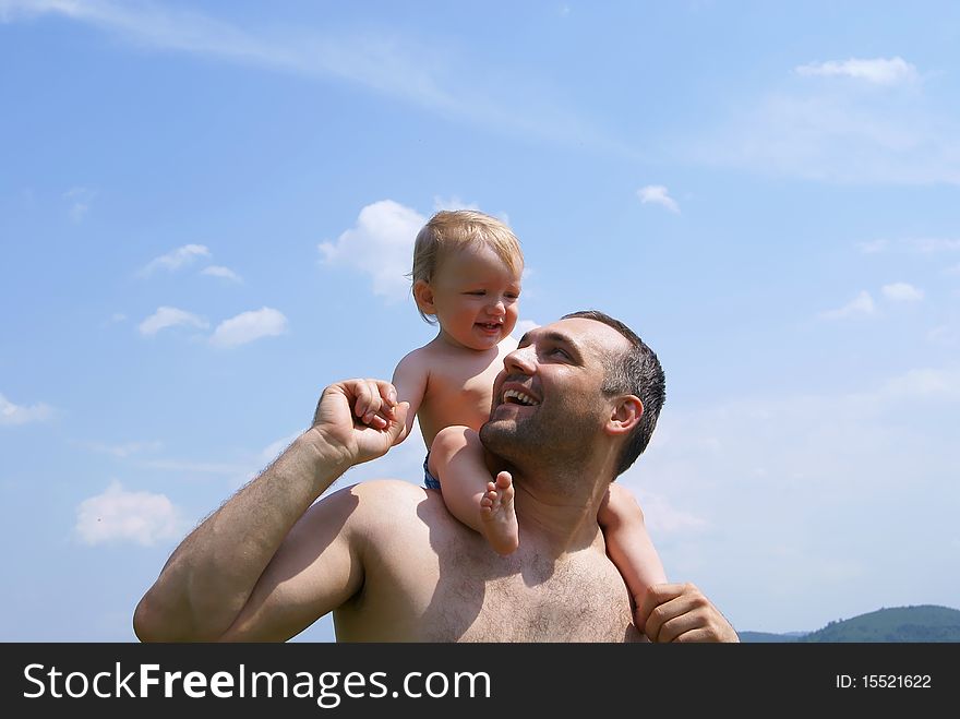 In the summer against the sky the man holds the baby for hands having put to itself on shoulders. In the summer against the sky the man holds the baby for hands having put to itself on shoulders