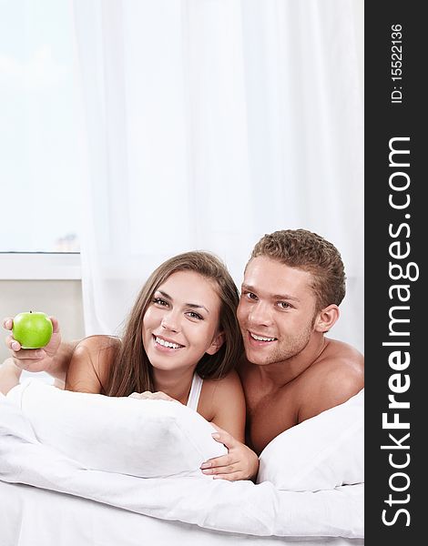 Young happy couple in bed with apple. Young happy couple in bed with apple