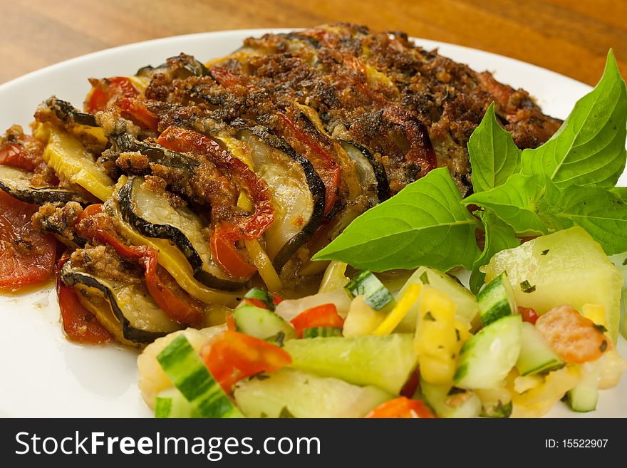 A baked meat and vegetable dish with a side salad of vegetables. A baked meat and vegetable dish with a side salad of vegetables