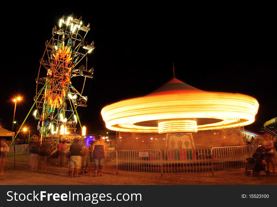 A view of the ferris wheel and merry go around in motion at the county fairgrounds night. A view of the ferris wheel and merry go around in motion at the county fairgrounds night