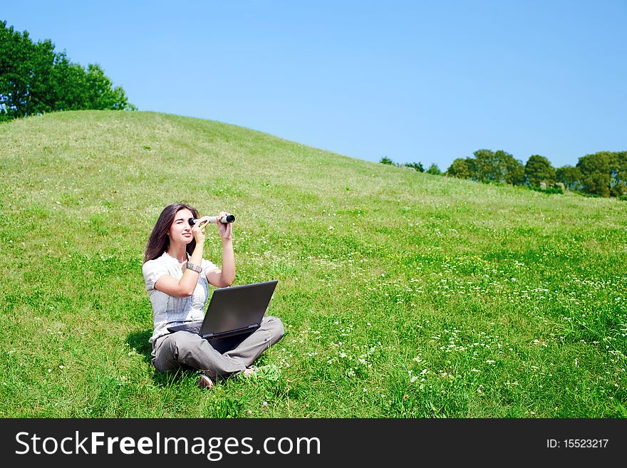 Beautiful young woman with spyglass and notebook on grass