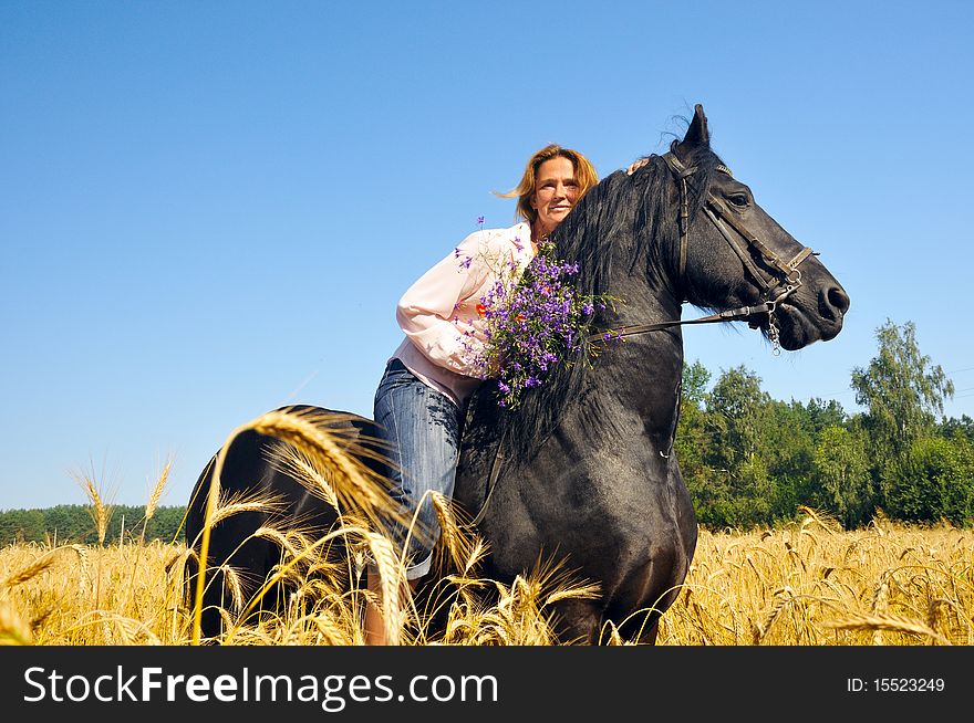 Beautiful smiling woman rides pretty black horse in field