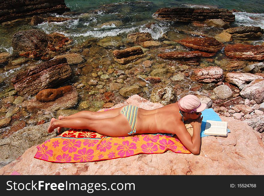 A girl is reading a book on a rocky beach in Montenegro. A girl is reading a book on a rocky beach in Montenegro