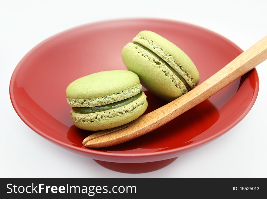 French Macarons served on a red plate with a wooden fork on white background. French Macarons served on a red plate with a wooden fork on white background.