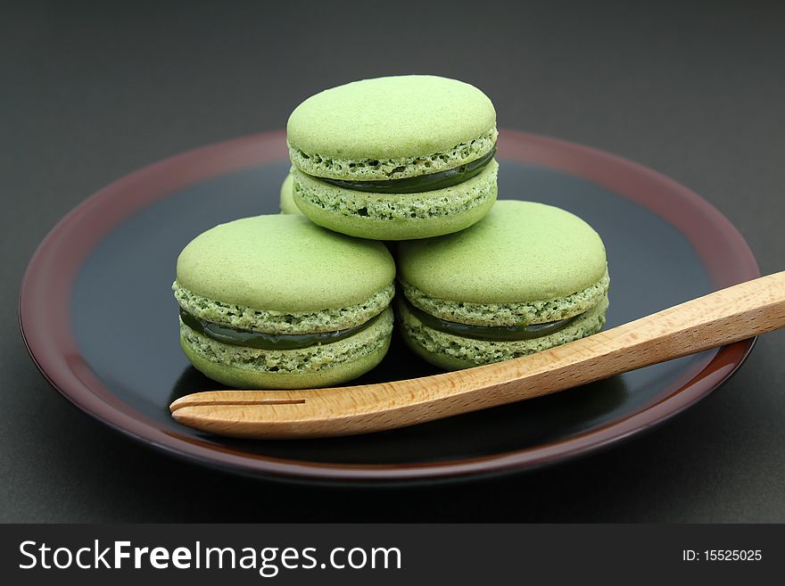French green tea Macarons served on a black and brown plate with a wooden fork on black background. French green tea Macarons served on a black and brown plate with a wooden fork on black background.