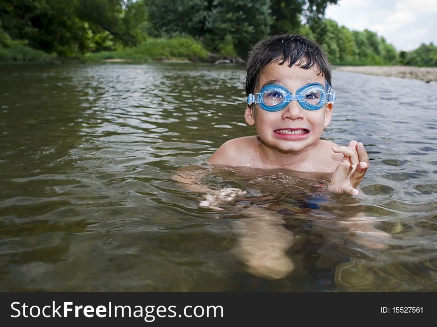 A young boy makes faces while playing in swim goggles in a clear creek. A young boy makes faces while playing in swim goggles in a clear creek.