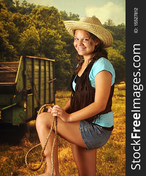 A happy young teen in cowgirl gear and shorts holding a rope in a field. A happy young teen in cowgirl gear and shorts holding a rope in a field.