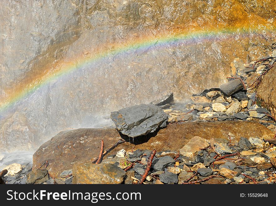 Rainbow over rocks under a small waterfall.