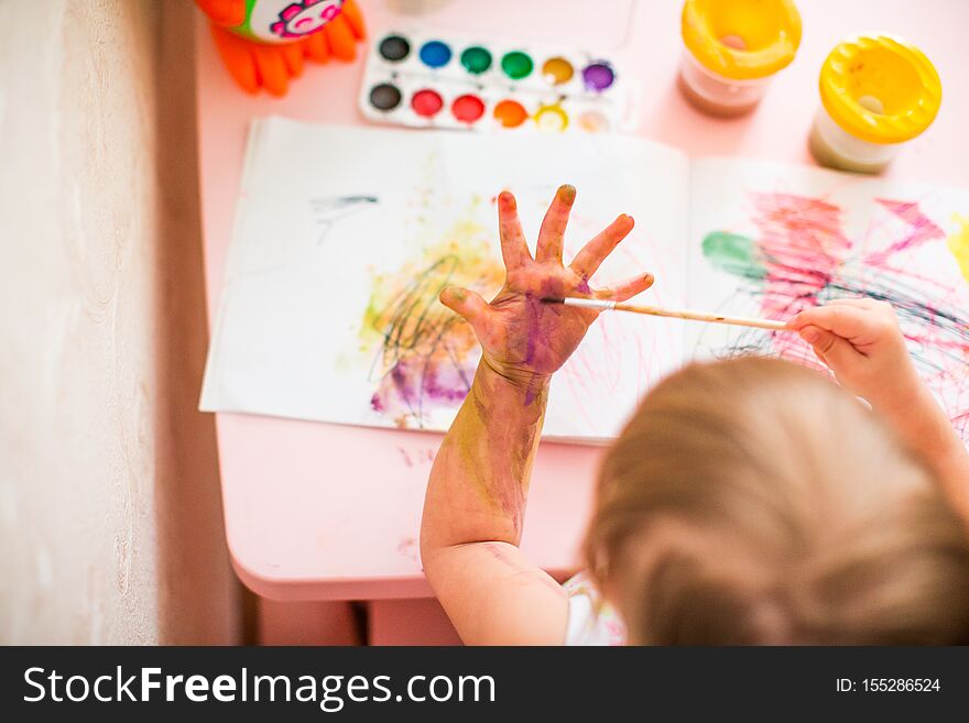 A hand of blonde baby girl drawing on her hand with watercolors. View from above
