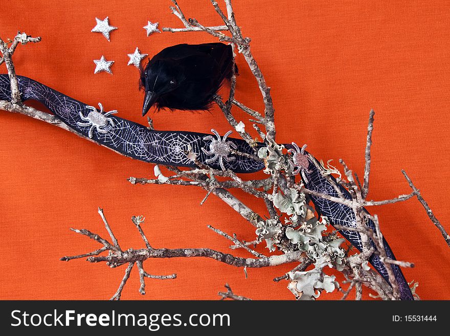 Halloween Raven on a dead branch with spiders and stars on an orange textile