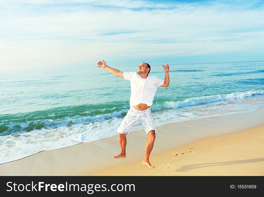 Happy man jumping on the beach at sunrise