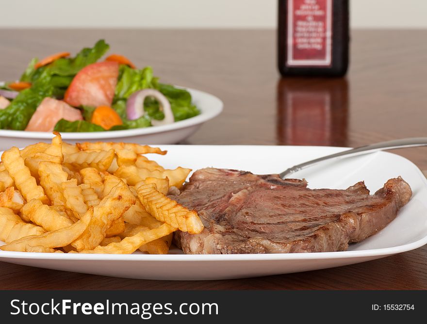 T-bone steak and french fries meal with a salad in the background. T-bone steak and french fries meal with a salad in the background