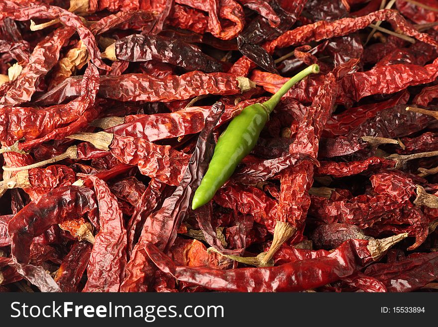 A conceptual shot of a single green chilly on top of red chillies. A conceptual shot of a single green chilly on top of red chillies